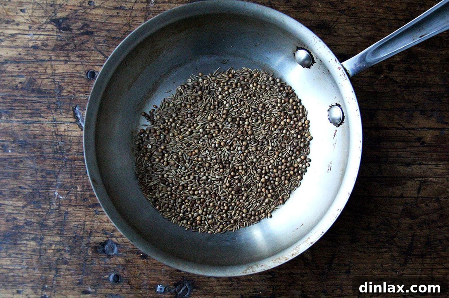 A skillet filled with whole cumin and coriander seeds, ready for toasting.