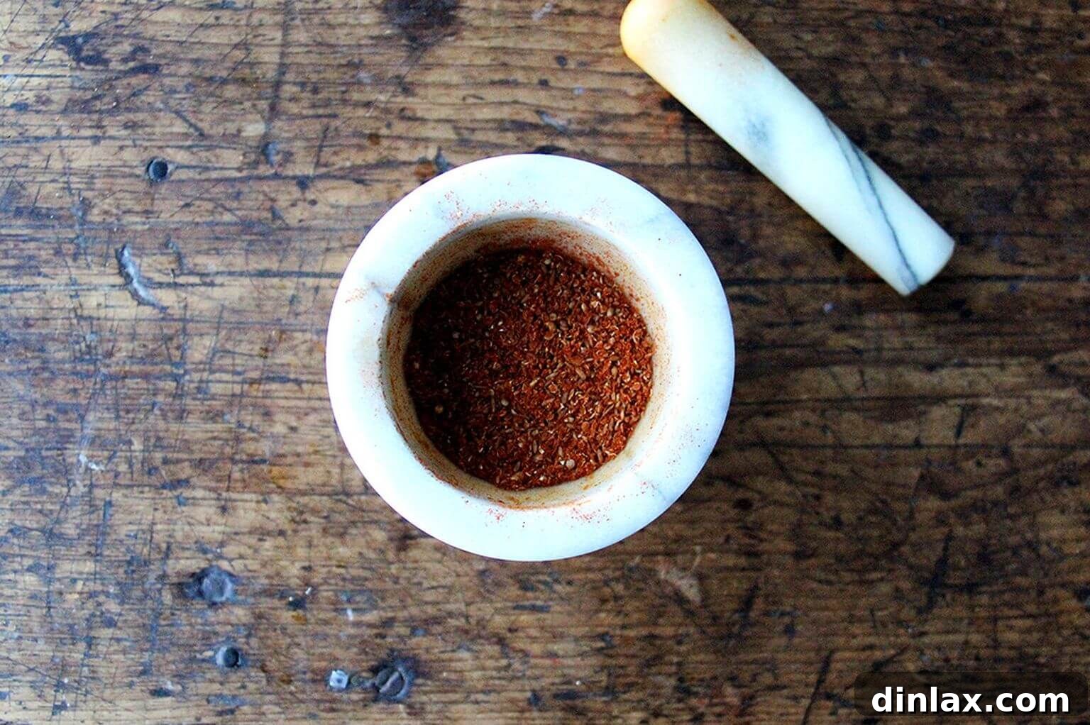 A mortar and pestle grinding freshly toasted shawarma spices, including cumin, coriander, smoked paprika, and cayenne.