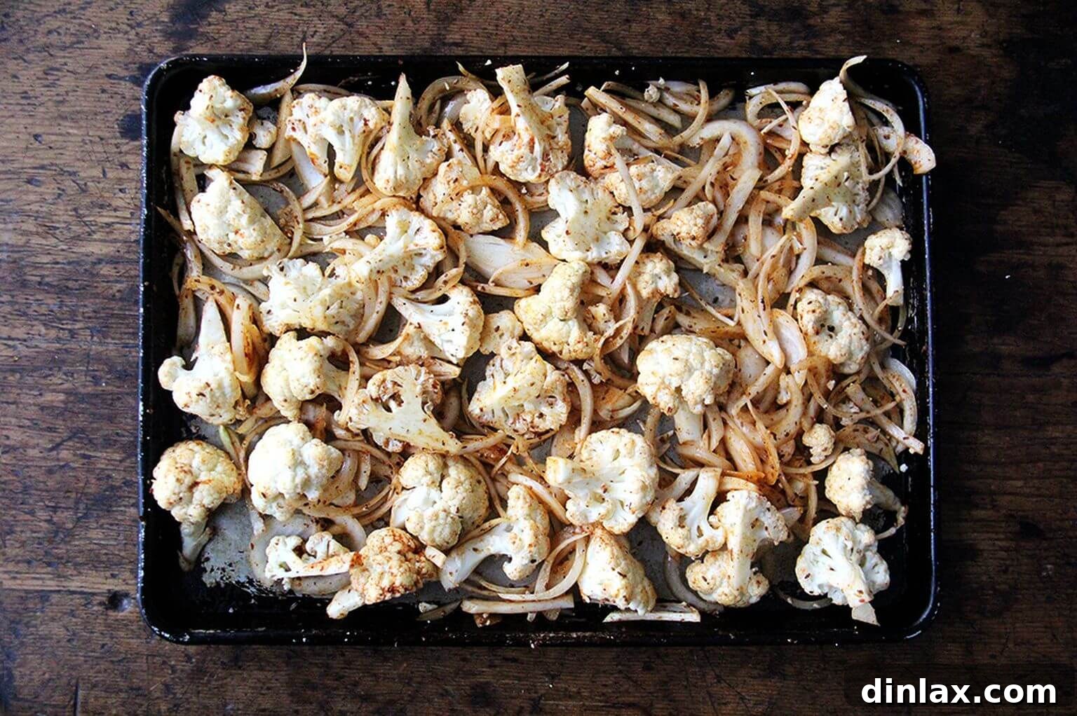 A sheet pan showcasing perfectly seasoned cauliflower florets and sliced onions, infused with shawarma spices, before roasting.