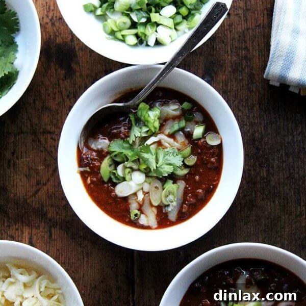 A bowl of super easy weeknight chili topped with fresh scallions and shredded cheddar cheese, ready to serve.