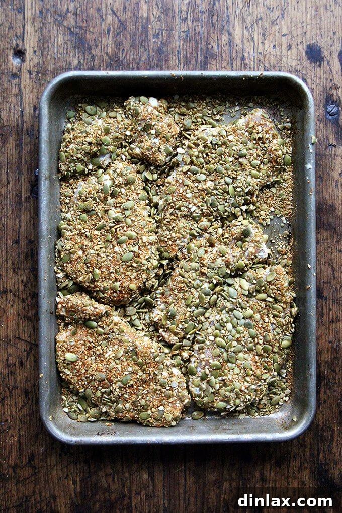 The breading process for Pepita-Crusted Chicken Cutlets, showing chicken being coated in the pumpkin seed and spice mixture.