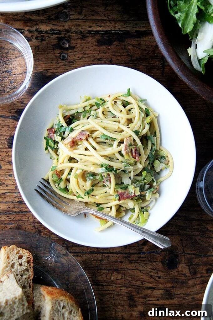 A beautifully plated dish of bucatini carbonara with leeks, lemon, and bacon, garnished with fresh parsley and a generous sprinkle of parmesan cheese, ready for a romantic Valentine's Day dinner.