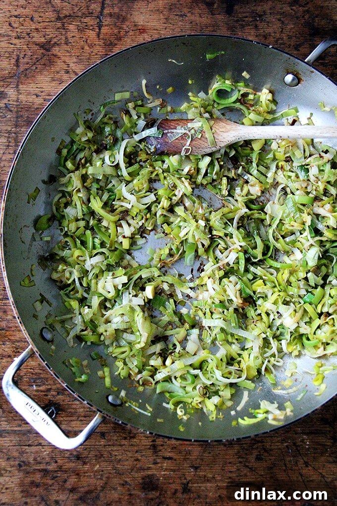 Sliced leeks being sautéed in a skillet, likely in bacon fat, to soften and caramelize for the bucatini carbonara recipe.
