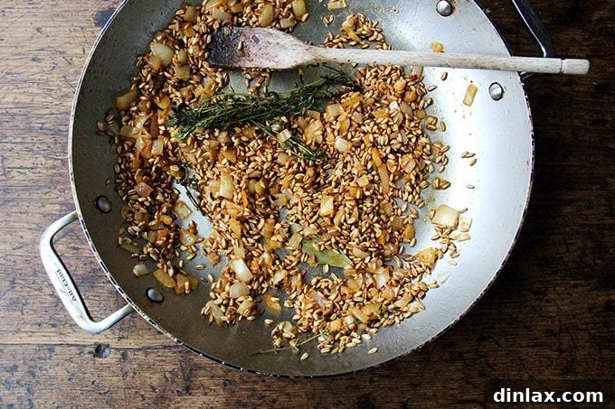 Mediterranean Farro Risotto with Kale and Feta 2 A sauté pan with golden onions, farro, fresh thyme sprigs, and a bay leaf simmering on the stovetop.