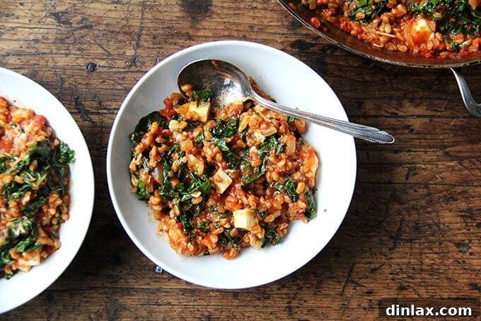Mediterranean Farro Risotto with Kale and Feta 7 A serving bowl of farro risotto with kale and feta, garnished and ready to be enjoyed, with a spoon nestled in.