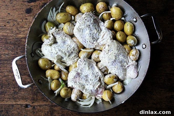 Sheet Pan Tarragon Chicken and Potatoes 6 A braiser filled with potatoes, onions, and seasoned chicken thighs, ready for roasting.
