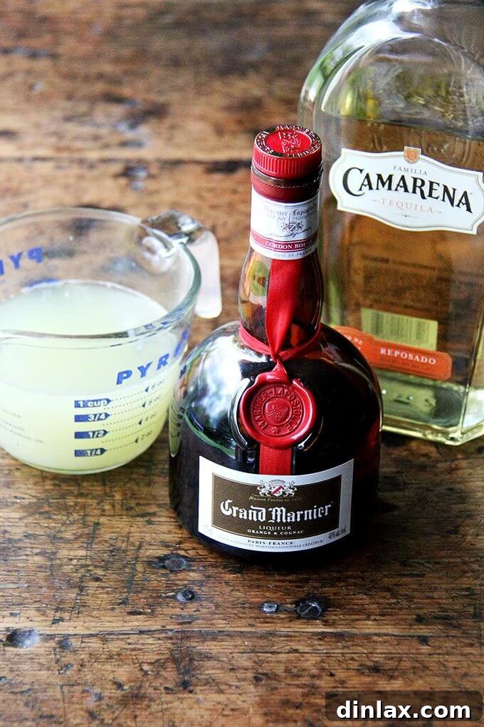 Individual ingredients for a classic margarita: fresh lime juice, Grand Marnier, and tequila lined up.