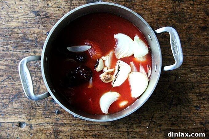 A pot of simmering tomatoes, broiled onions, garlic, and chipotles in adobo.