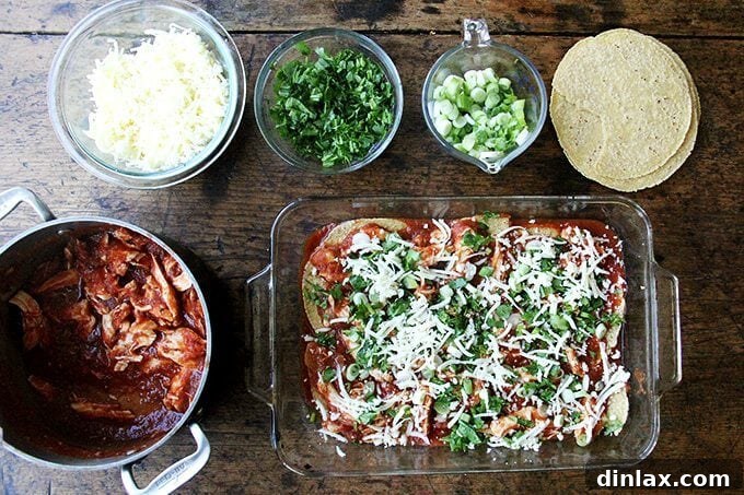 An assembled chicken enchilada casserole, layered with tortillas, sauce, chicken, and cheese, ready for baking.