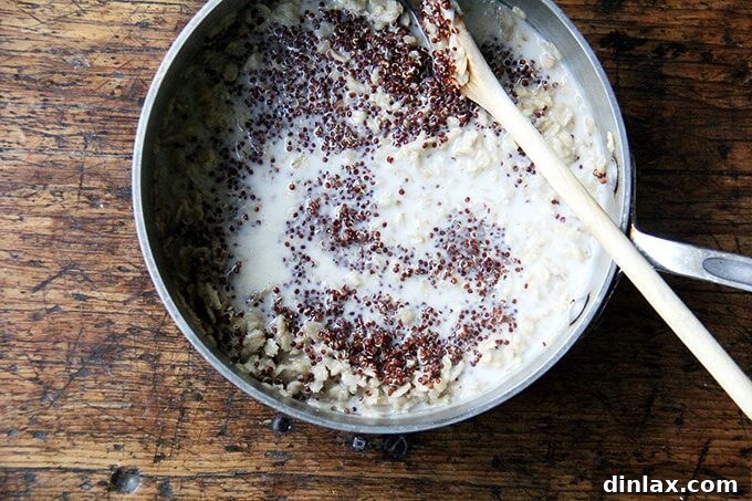 Uniting Oats, Quinoa, and Spiced Almond Milk for a Delicious Porridge A close-up of a spoon gently mixing cooked oats and quinoa with the infused almond milk in a saucepan, creating a creamy and aromatic breakfast porridge mixture.