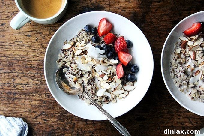 Garnishing the Perfect Oat and Quinoa Porridge with Fresh Toppings A hand garnishing a bowl of healthy Oat and Quinoa Porridge with fresh berries and nuts, prepared for a satisfying and nutritious breakfast, alongside a steaming cup of coffee.