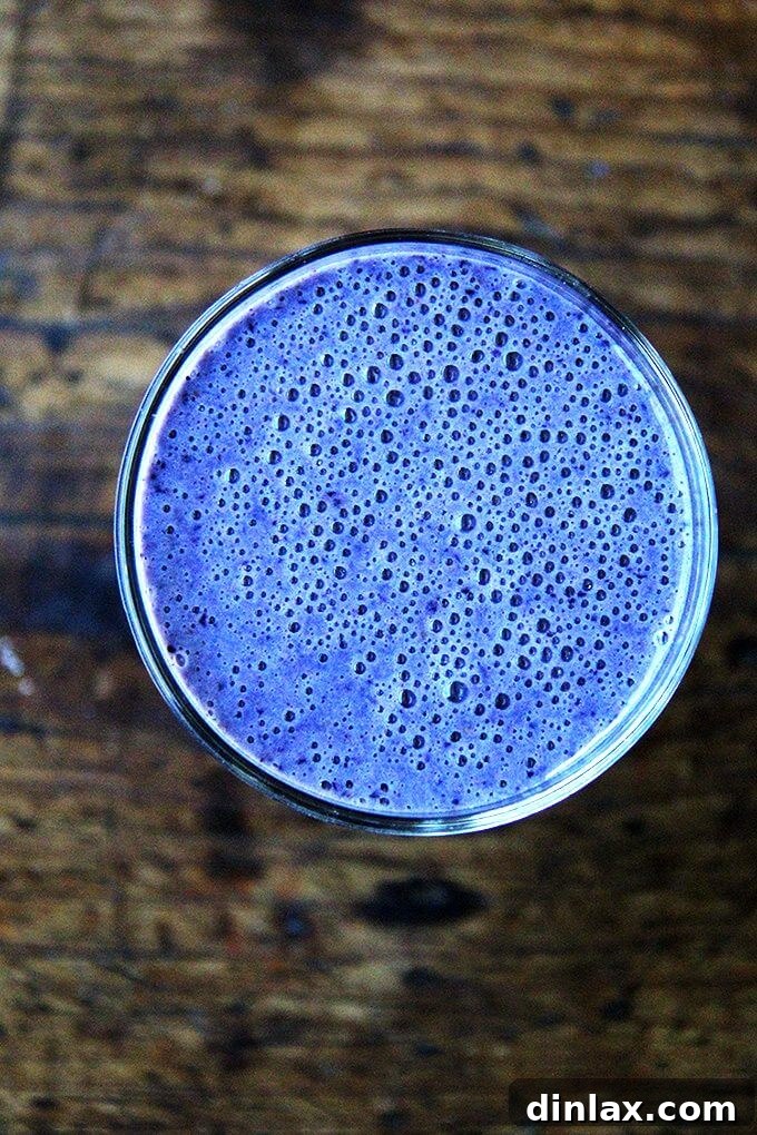 Blueberry Almond Vitality Smoothie 2 Overhead shot of a vibrant blueberry smoothie in a clear glass, garnished with fresh blueberries and a mint leaf.