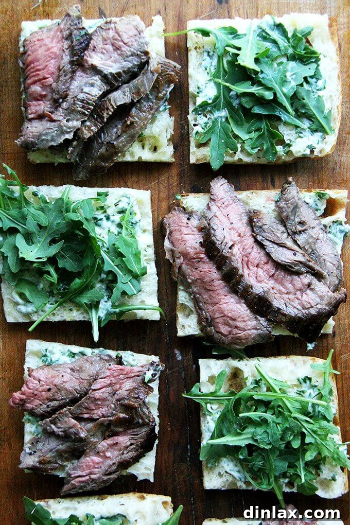 Layering ingredients for a gourmet skirt steak sandwich. Assembling a skirt steak sandwich with herbed mayonnaise, tender steak, and fresh arugula on focaccia.