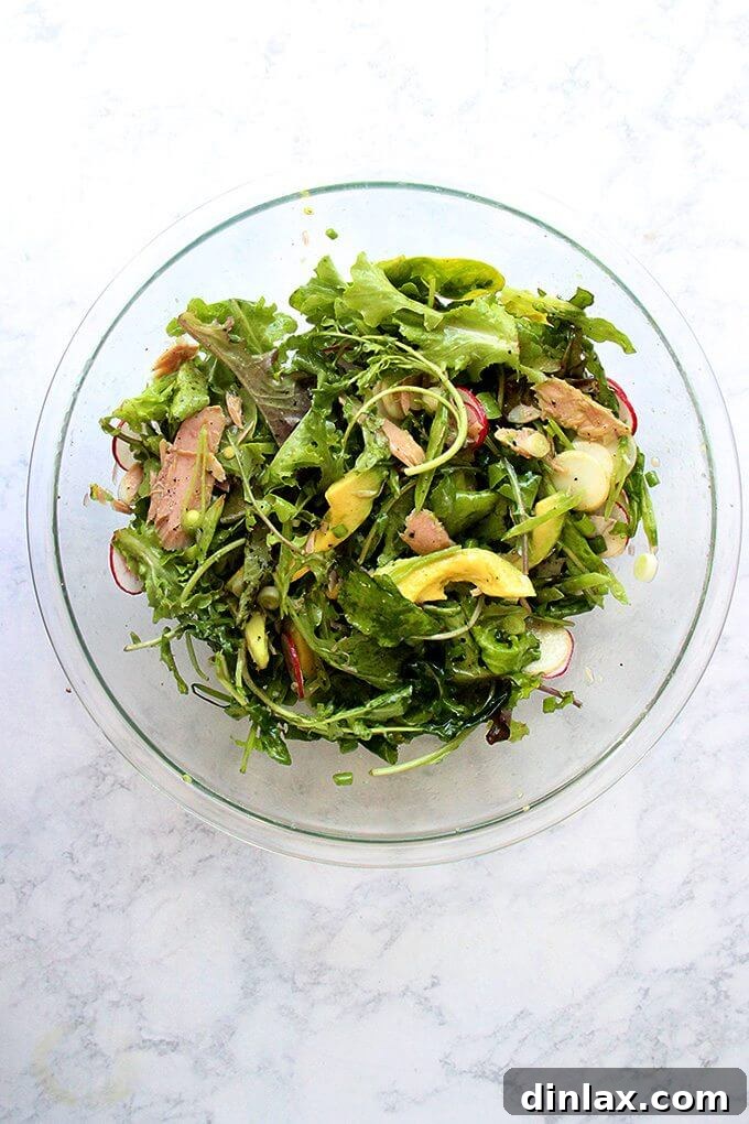 10-Minute Tuna and Greens Salad with Shallot Vinaigrette 4 A large, vibrant salad bowl, perfectly tossed, featuring a medley of fresh greens, thinly sliced radishes, rich avocado, and tender jarred tuna, all evenly coated in a bright shallot vinaigrette.