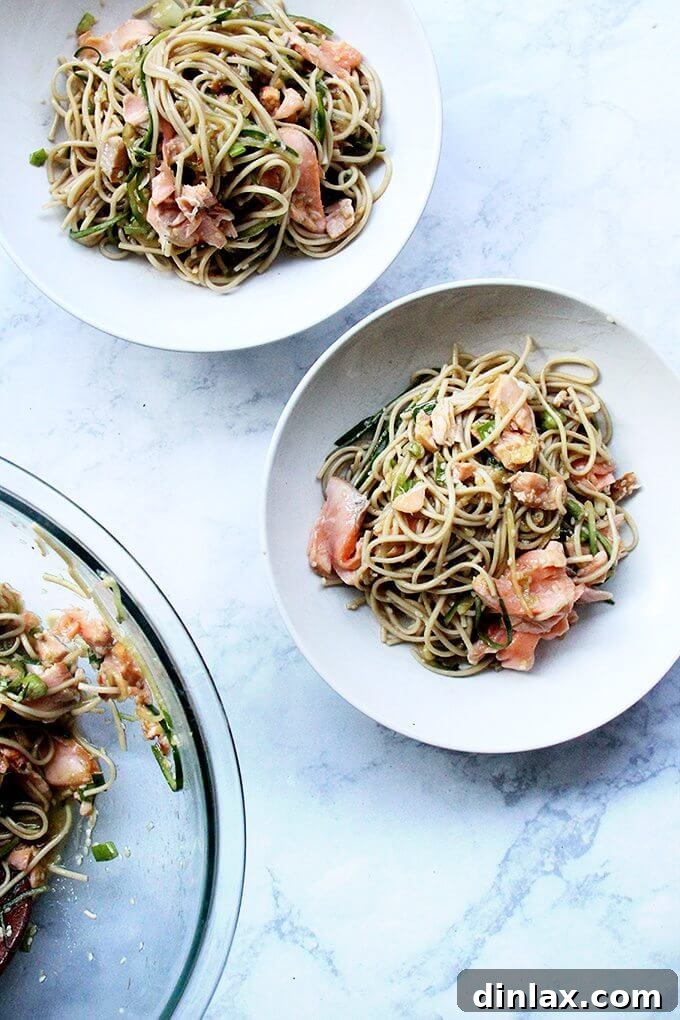 One sauce, two roles—a revelation! With dinner prep (and clean up) decreased by half, this recipe for ginger-sesame soba noodles with cedar plank salmon slips into weeknight-friendly territory, requiring about 30 minutes of work. // alexandracooks.com Two vibrant bowls of ginger-sesame soba noodles topped with pieces of cedar plank salmon, ready to serve.