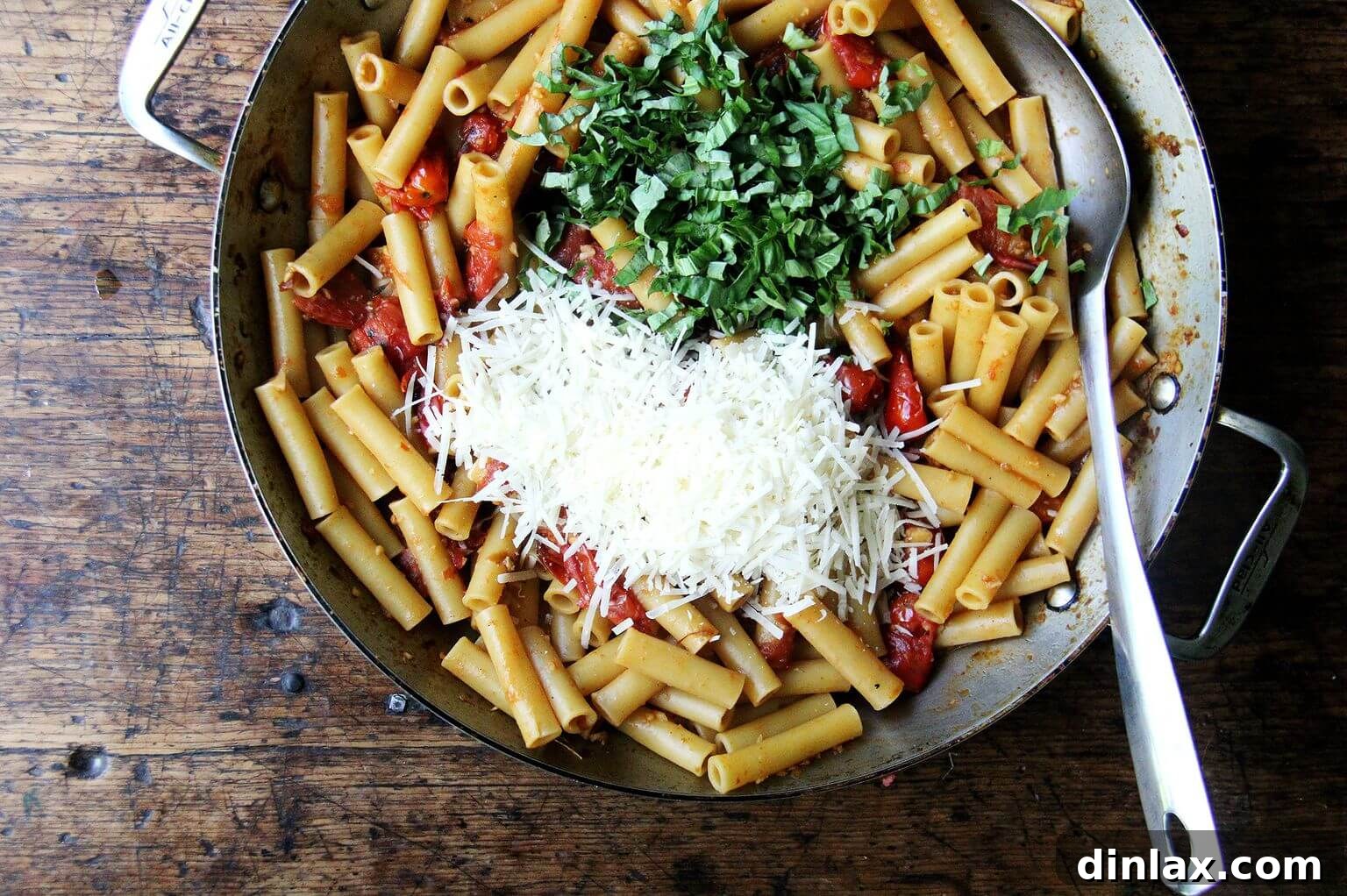A large skillet brimming with cooked ziti, generously mixed with grated Parmesan cheese and fresh basil leaves, ready for the final topping.
