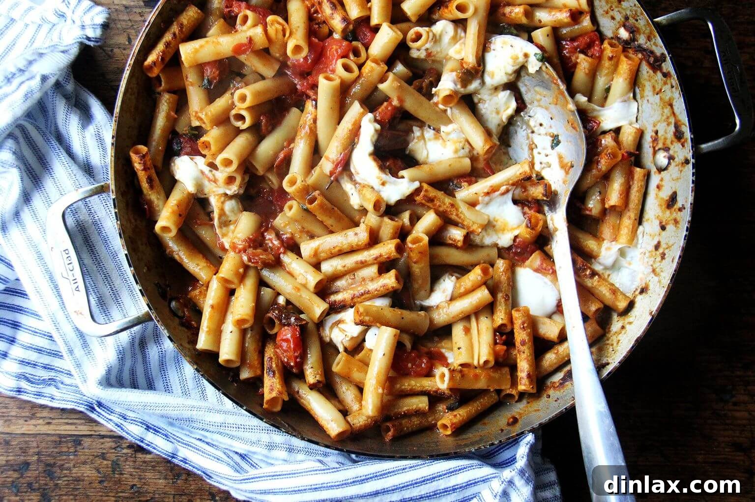 A large skillet of one-pan baked ziti, with a serving spoon nestled in, inviting a hearty portion.