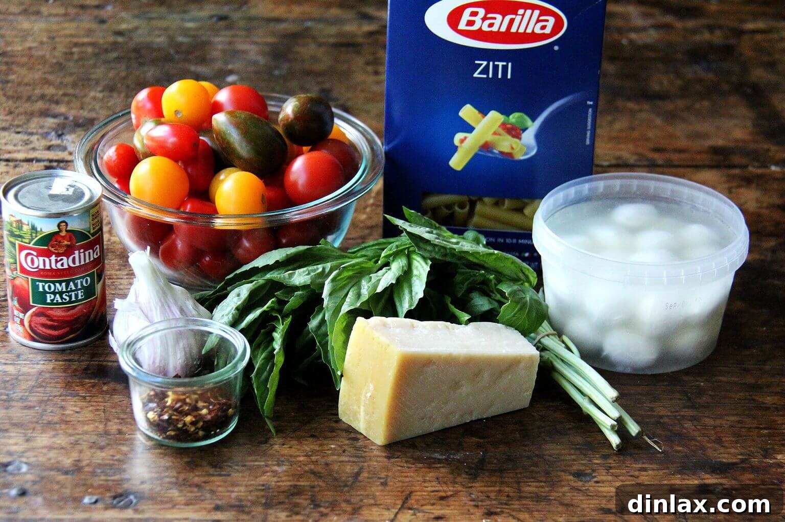 Essential ingredients neatly arranged for a simple one-pot baked ziti recipe, including pasta, tomatoes, cheese, and herbs.