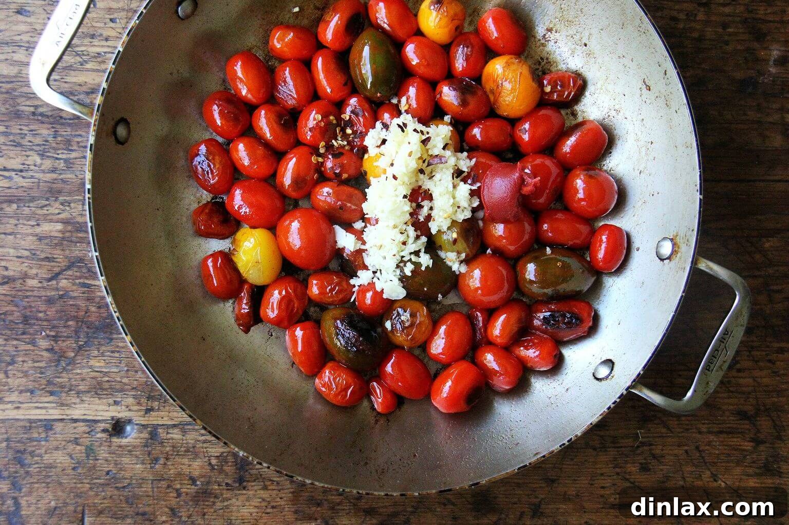 A large skillet containing glistening cherry tomatoes and thinly sliced garlic, simmering to create a fragrant base.