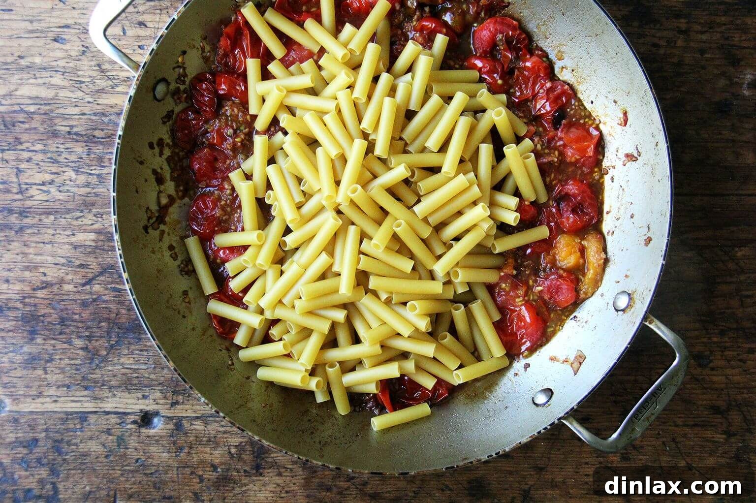 Uncooked ziti pasta is added directly into the simmering tomato sauce, ready to absorb flavors as it cooks.