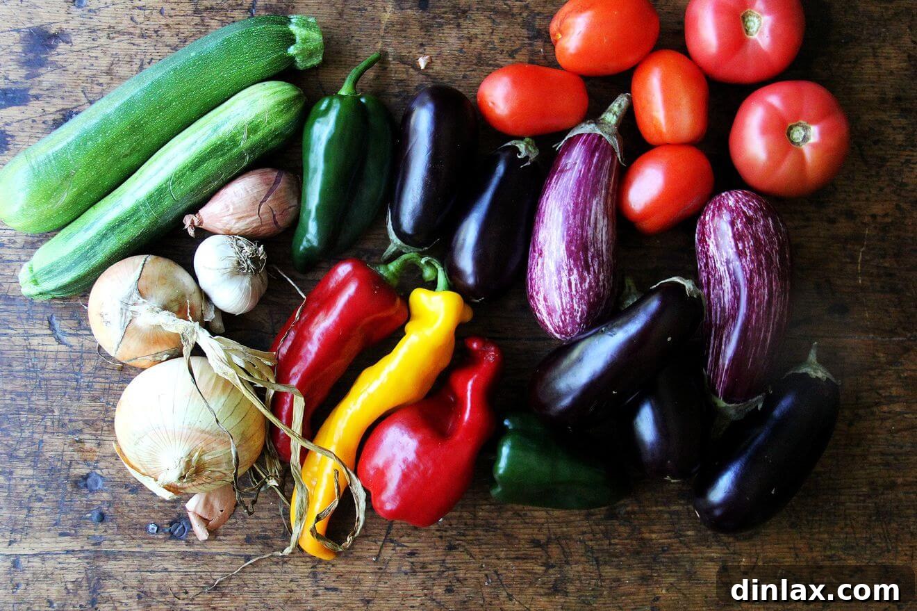 A vibrant assortment of fresh, raw ratatouille vegetables, including tomatoes, eggplant, zucchini, peppers, and onions, neatly arranged on a wooden board before chopping.