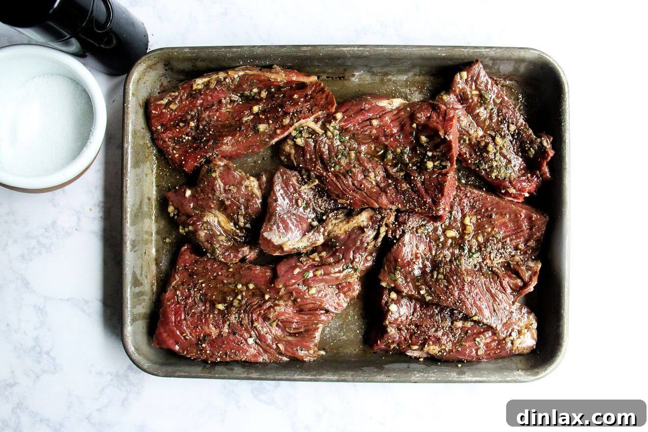 Marinated hanger steaks seasoned with salt and pepper on a sheet pan, prepared for grilling.