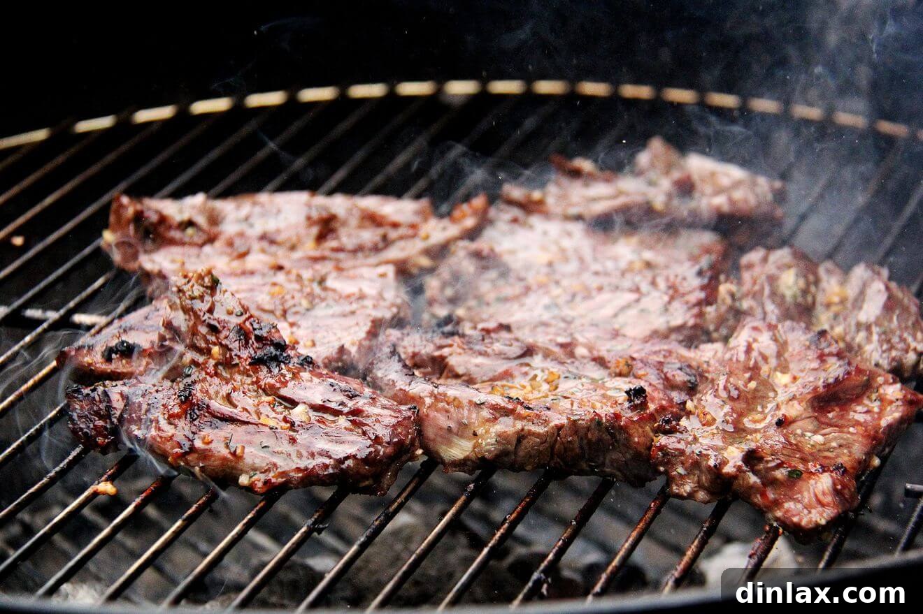 Hanger steaks sizzling on the hot grates of a charcoal grill, developing a perfect crust.