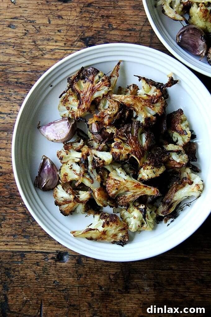 A vibrant plate of golden oven-roasted cauliflower florets, caramelized onions, and whole roasted garlic cloves, sprinkled with crisp Parmesan cheese.