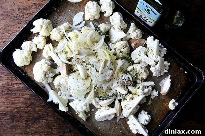 Cauliflower florets, sliced onions, whole garlic cloves, and thyme sprigs tossed with olive oil, salt, and pepper on a baking sheet, glistening and ready for the oven.