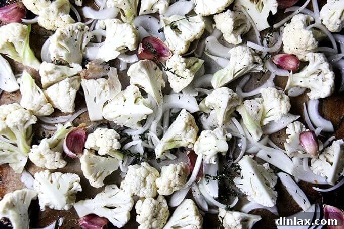 A baking sheet with cauliflower, onions, garlic, and thyme spread out in a single layer, perfectly arranged and ready to be placed in the hot oven.