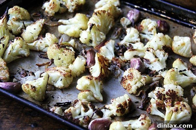 Oven-roasted cauliflower florets on a sheet pan, now tender and slightly golden, with onions beginning to caramelize after the initial roasting period.