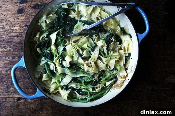 An overhead shot of pasta carbonara being tossed in a skillet, the creamy sauce coating the pasta and greens evenly.