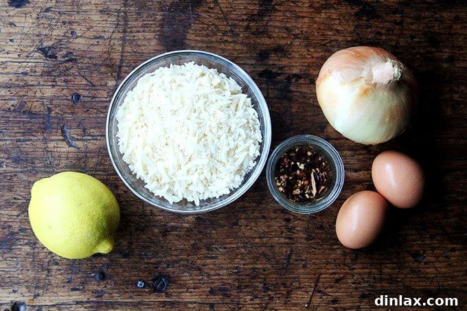 A collection of carbonara sauce ingredients laid out on a table: a fresh lemon, a bowl of grated Parmesan cheese, a whole onion, red pepper flakes, and two eggs.