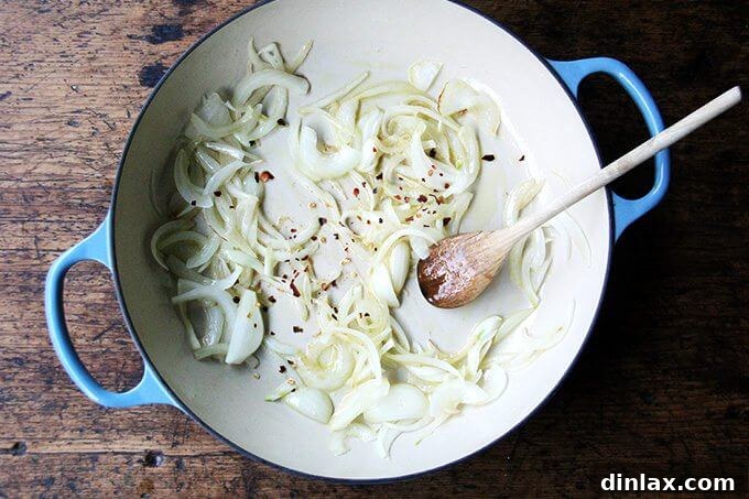 An overhead shot of thinly sliced onions being sautéed in a skillet, with a sprinkle of crushed red pepper flakes adding a hint of spice.