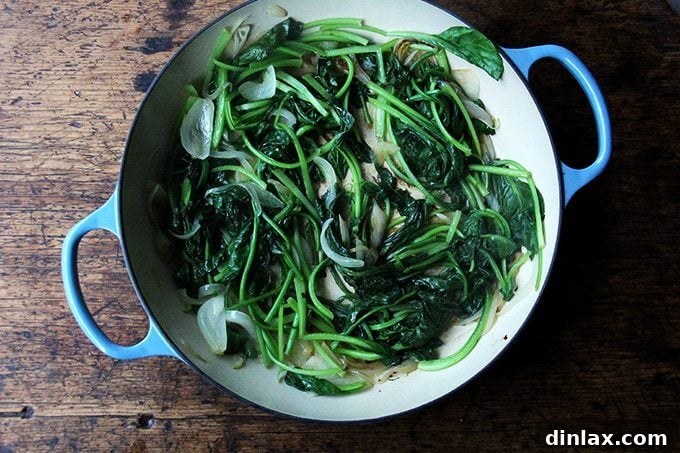 An overhead shot of a skillet showing a heap of leafy greens, now sautéed and considerably wilted, mixed with the onions.