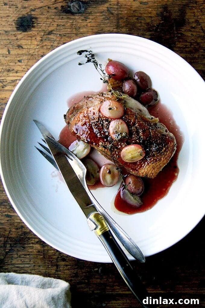 A beautifully plated dish of sliced duck breast, gastrique sauce, roasted grapes, and fresh thyme sprigs.