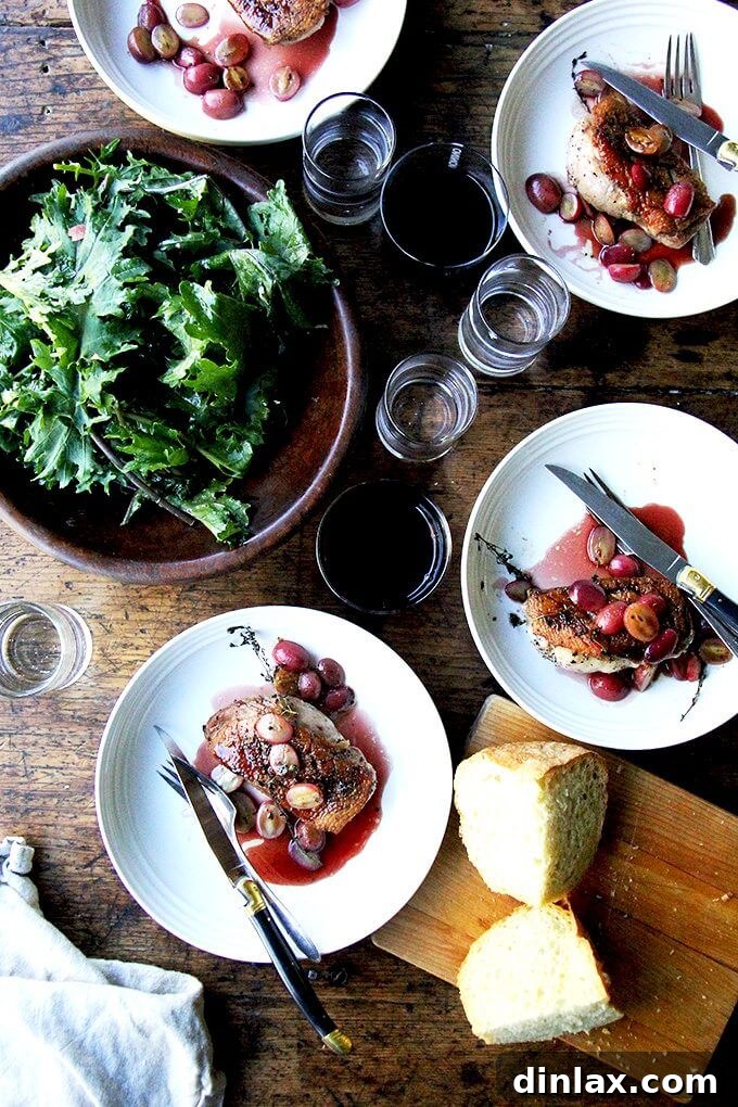 An overhead shot of a dining table elegantly set with four plates of duck breast, alongside fresh salad, crusty bread, wine, and water.