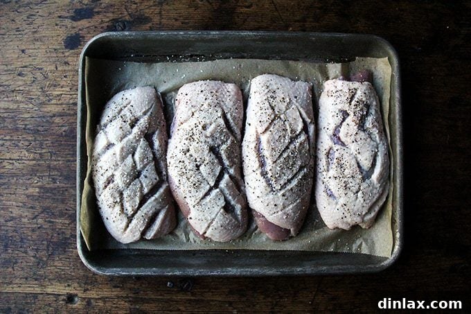 Four duck breasts with their fat scored in a diamond pattern, ready for cooking.