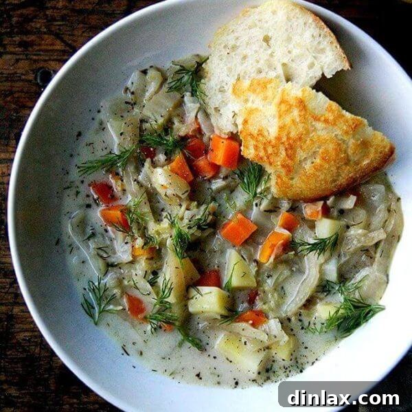 A close-up shot of a rustic bowl of hearty vegetarian cabbage soup, garnished with fresh green dill, served with a slice of golden crusty bread.