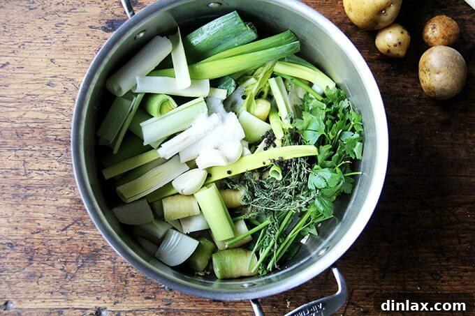 A large pot filled with an assortment of fresh vegetables including leeks, onions, carrots, celery, and herbs, simmering to create homemade vegetable stock.