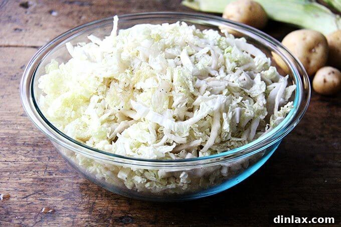 A large ceramic bowl generously filled with thinly sliced green cabbage, ready for preparation.