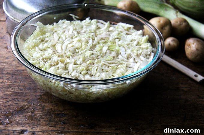 A large bowl brimming with thinly sliced green cabbage, now covered with steaming hot water, indicating the blanching process has begun.