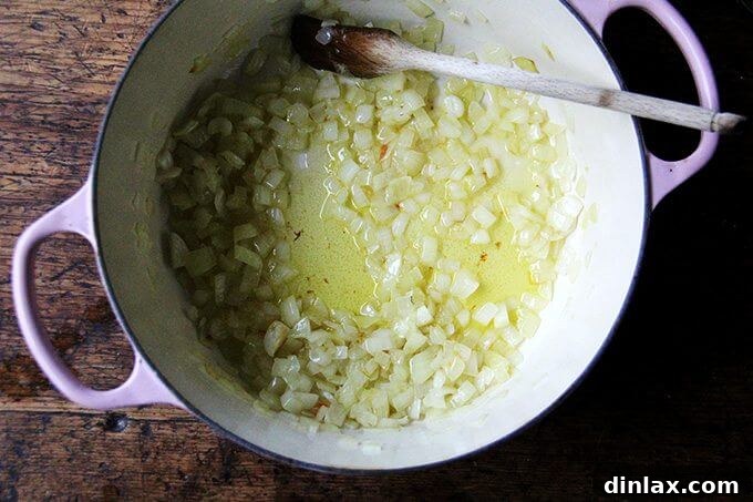An overhead shot showing diced onions gently sautéing in a large pot with olive oil on a stovetop, their edges beginning to soften and caramelize.