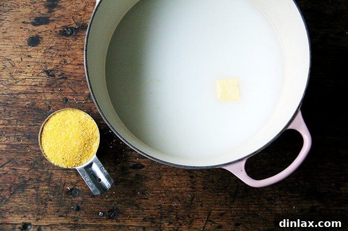 A Dutch oven on the stovetop, showcasing the initial mixture of water, milk, and a substantial pad of butter, ready to be combined with polenta before baking.