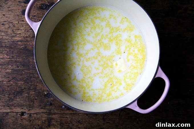 A Dutch oven containing the meticulously whisked mixture of water, milk, polenta, and butter, perfectly prepared and ready to be transferred to the oven for baking.