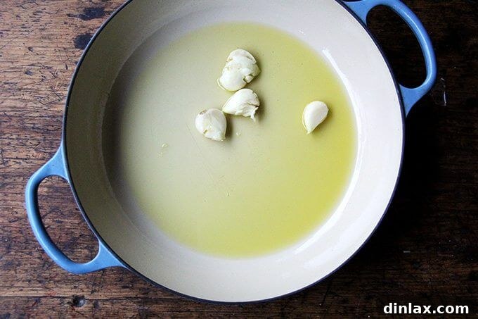 A braiser on the stovetop, filled with shimmering oil and fragrant whole garlic cloves, the starting point for preparing delicious caramelized cabbage.