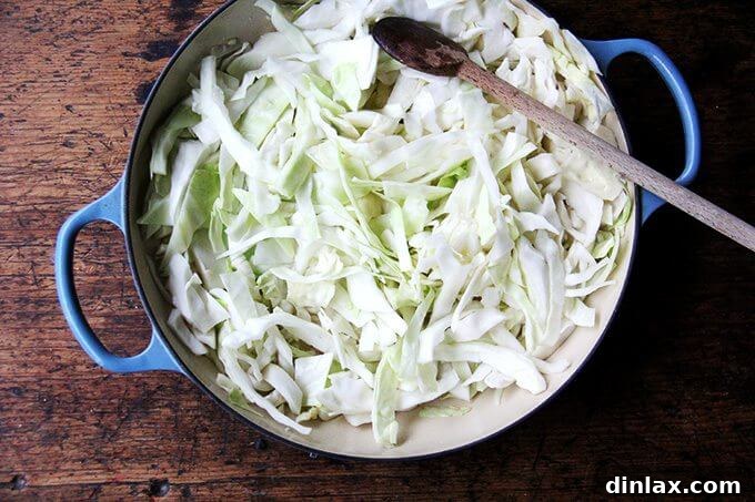 A braiser generously filled with freshly chopped cabbage, slowly beginning to soften and caramelize as it cooks, releasing its natural sweetness.