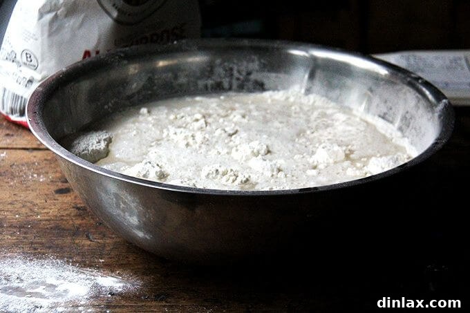 A sticky dough ball resting in a large mixing bowl, covered for its first rise.