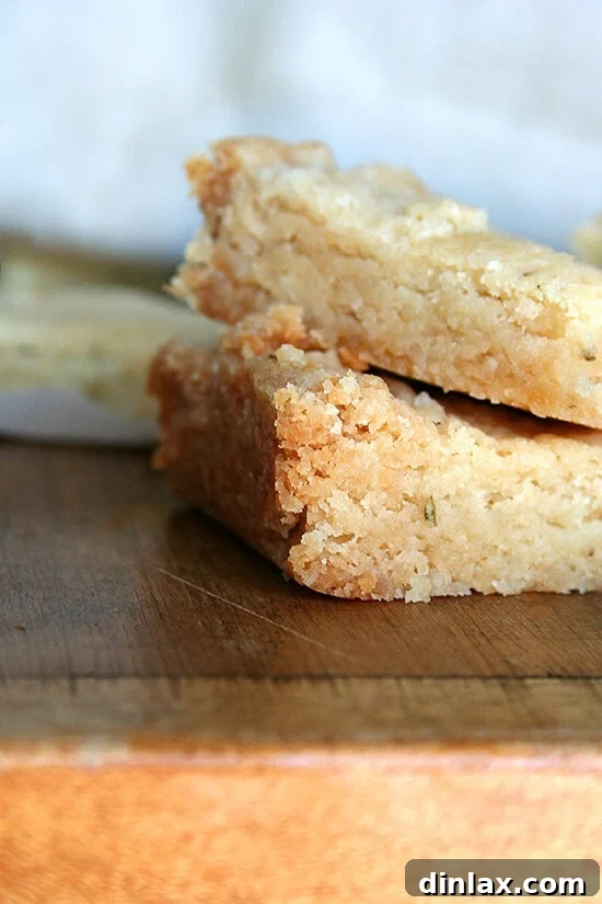 Elegant rosemary shortbread cookies artfully arranged on a cutting board, garnished with sprigs of fresh rosemary.