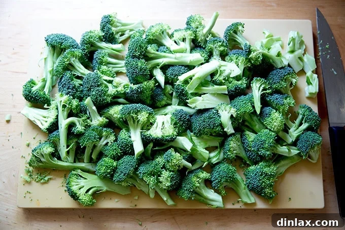 Ina Garten's Crispy Lemon Garlic Parmesan Roasted Broccoli 3 A wooden cutting board neatly topped with an abundance of freshly chopped broccoli florets, perfectly sized for roasting.